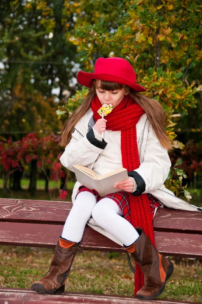 Beautiful girl sitting on a bench reading a book. — Stock Photo, Image