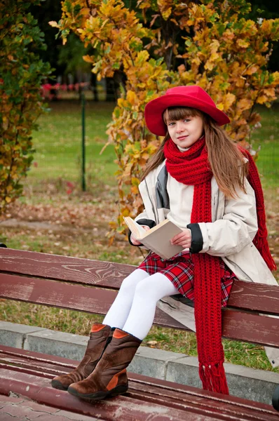 Beautiful girl sitting on a bench reading a book. — Stock Photo, Image