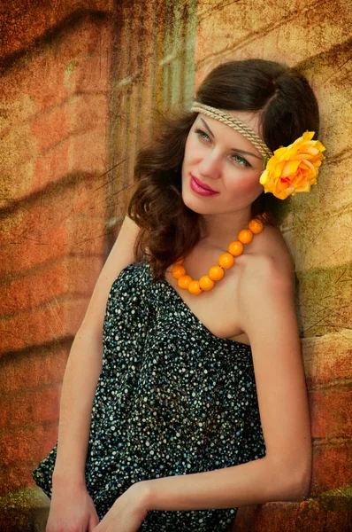 Mooie brunette met bloem in het haar tegen een bakstenen muur. — Stockfoto