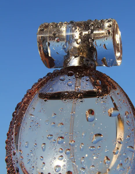 Garrafa de perfume em um fundo azul com gotas de água — Fotografia de Stock