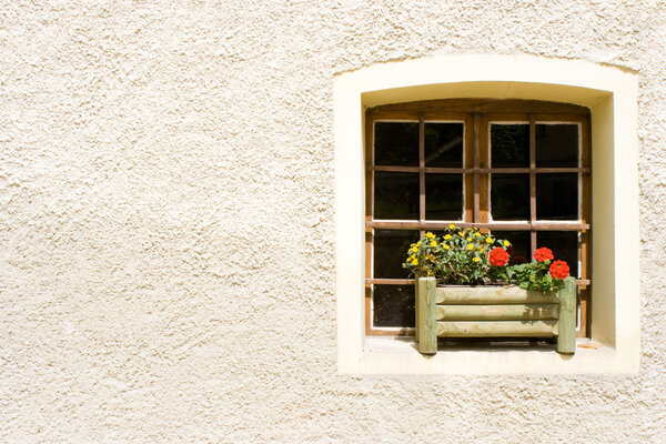 Rural window with red and yellow geranium flowers in a wooden vase. Plastered wall background.