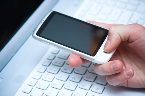 Smart phone in hand with laptop keyboard backgroun — Stock Photo, Image