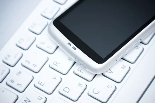 Teléfono inteligente sobre teclado blanco — Foto de Stock