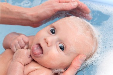 Newborn baby boy in bath puts out the tongue clipart