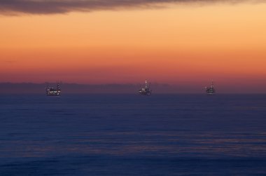 Offshore Oil Rig Drilling Platforms at Sunset clipart