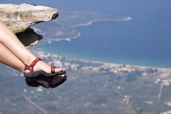 Woman with trekking sandals sitting on rock high above the sea — Stock Photo, Image