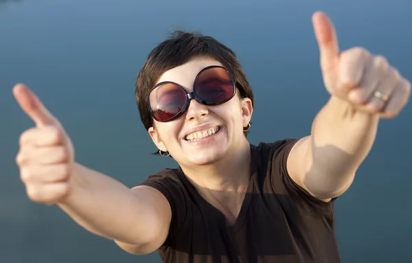Menina morena nova com grandes óculos de sol engraçados fazendo polegares para cima gesto — Fotografia de Stock