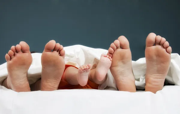 Mutlu ailenin iki bacağı yatakta - baba, anne ve bebek — Stok fotoğraf