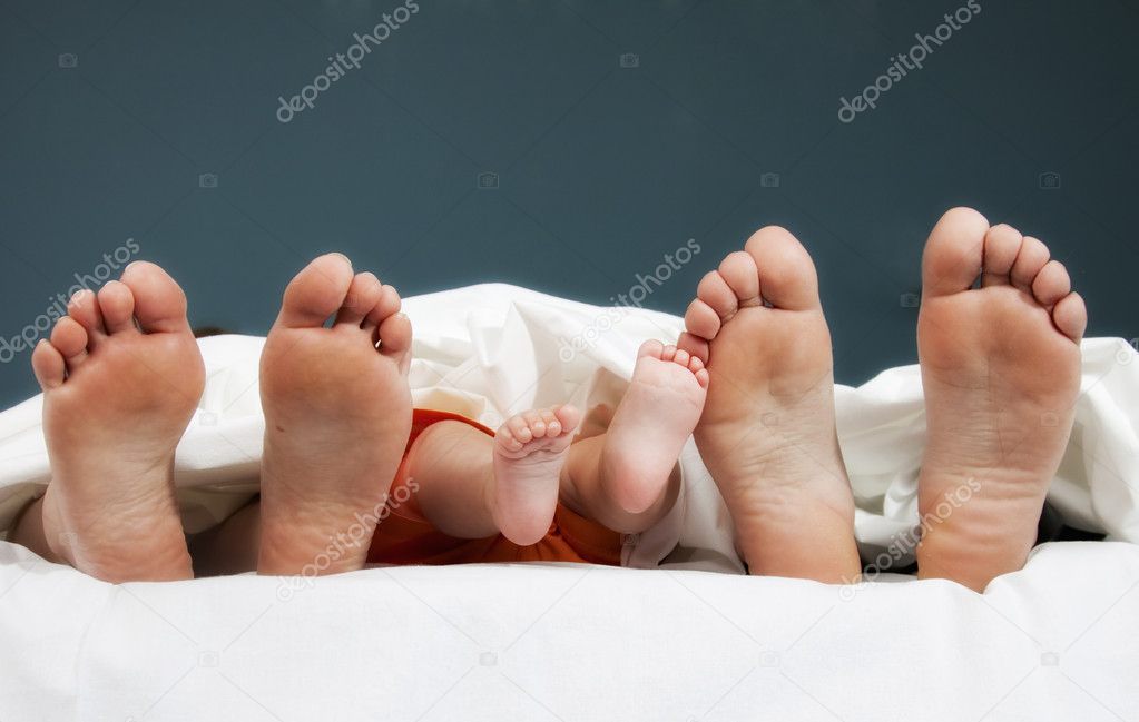 Tree pairs of legs of the happy family in bed - father, mother and baby