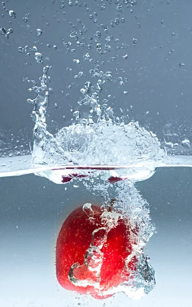 stock image Red apple splashing into water on blue background