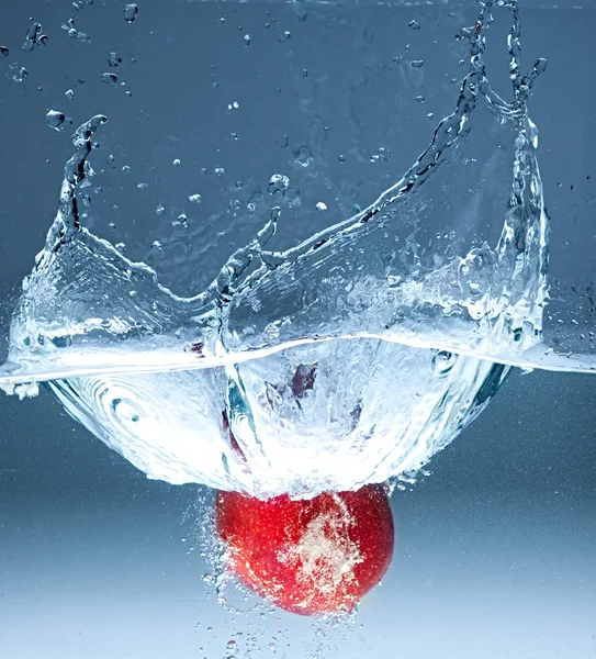 Red apple splashing into water on blue background — Stock Photo, Image