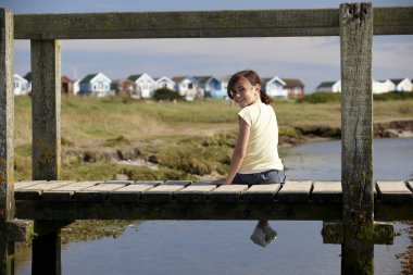 Girl sitting on bridge smiling at camera clipart