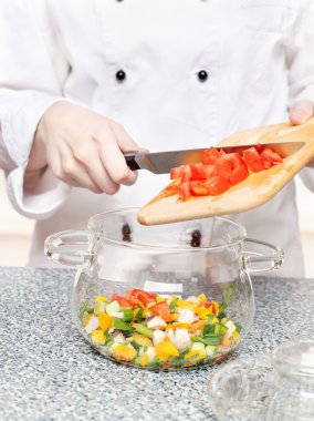 Chef adds chopped tomatoes in a glass bowl clipart