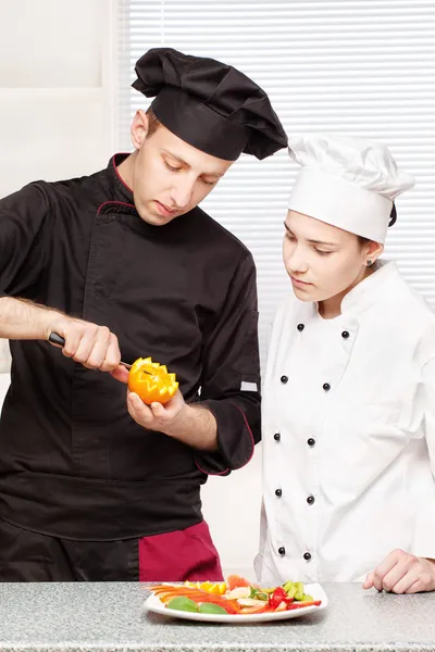 Старший повар учит молодого повара украшать фрукты — стоковое фото