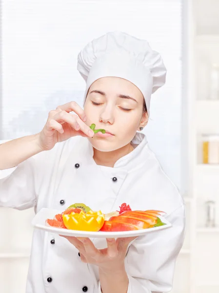 Шеф-повар нюхает мяту перед тем, как положить ее на тарелку с фруктами — стоковое фото