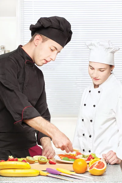 Senior chef teaches young chef to decorate fruit