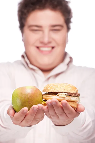 Пухкий чоловік тримає яблуко і гамбургер Стокове Зображення