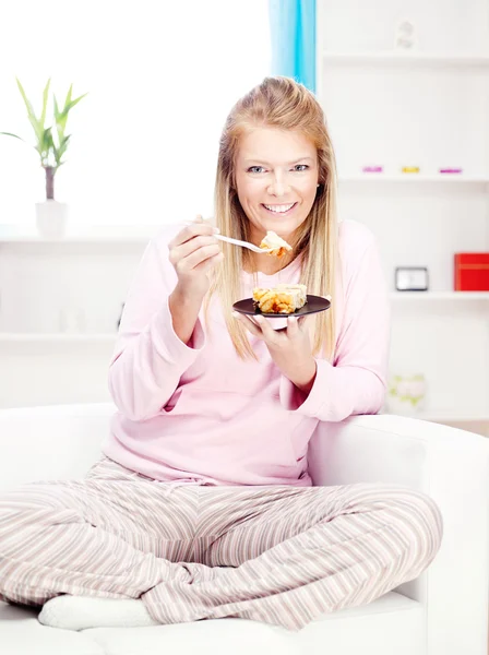 Vrouw op sofa eten taart thuis — Stockfoto