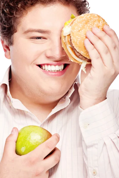 Young chubby man holding apple and hamburger — Stock Photo, Image