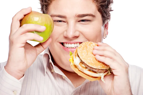 Obtloustlý mladík drží jablko a hamburger — Stock fotografie
