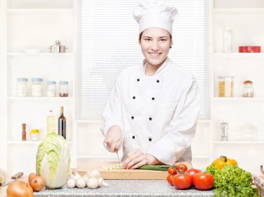 Female chef cutting onions on the cutting board in kitchen clipart