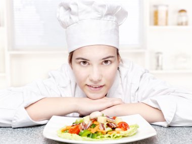 Pretty young chef and hers plate of a delicious salad in kitchen clipart