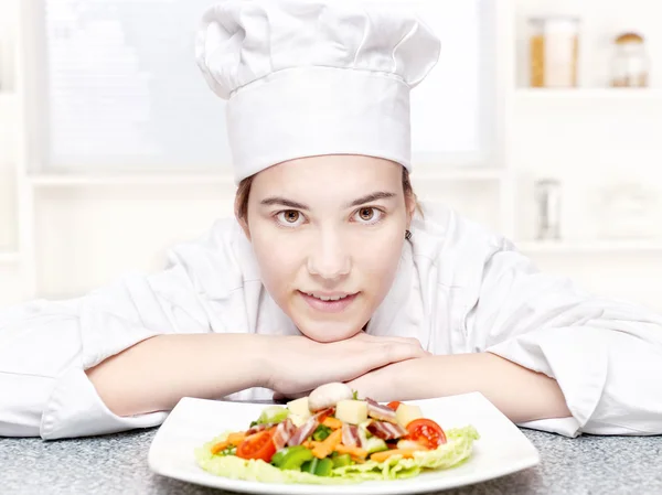 Симпатичный молодой шеф-повар и ее тарелка вкусного салата на кухне — стоковое фото