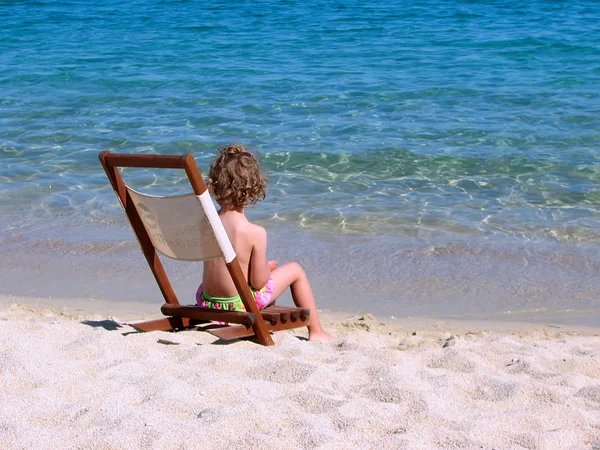 Kid sitting on the chair on the shore — Stock Photo, Image
