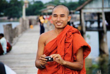 Myanmar monk taking a photo to a tourist on U-Bein bridge in Man clipart