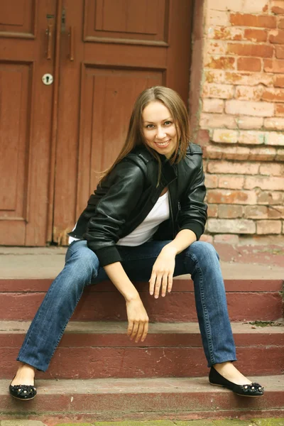 Dívka v černém kabátku sedí na verandě kroků — Stock fotografie