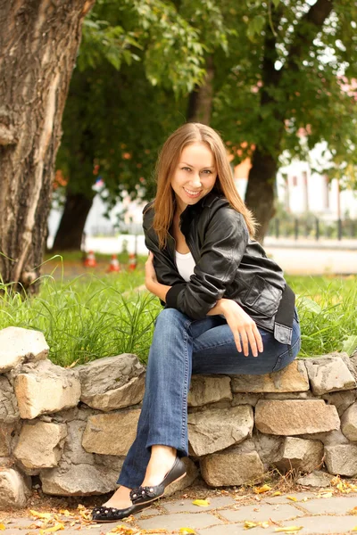 A menina em uma jaqueta preta senta-se em pedras no quadrado — Fotografia de Stock