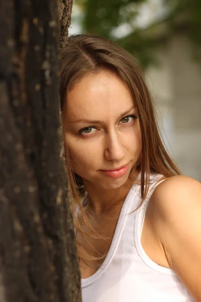 The girl in a white vest against a tree — Stockfoto