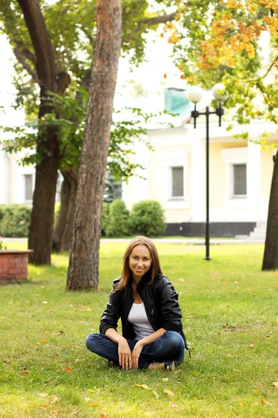 Flickan sitter på en gräs i parken — Stockfoto