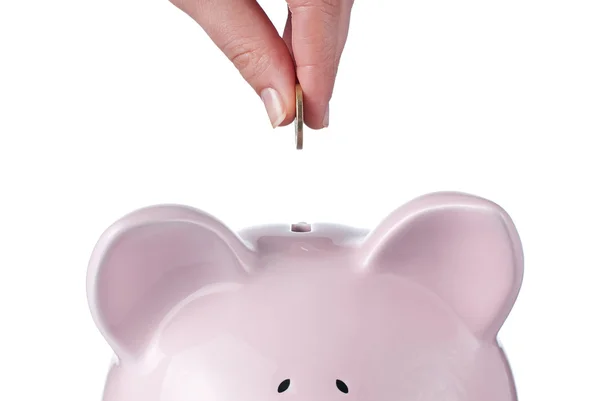 Mão das mulheres coloca uma moeda para o banco piggy rosa no fundo branco, S — Fotografia de Stock