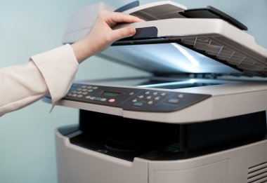 Woman's hand with working copier (focus on finger) clipart