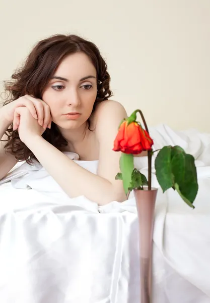 Kobieta w łóżku patrząc na róży — Zdjęcie stockowe