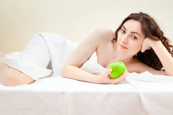 Piękna kobieta, leżąc w łóżku z zielonym jabłkiem — Zdjęcie stockowe