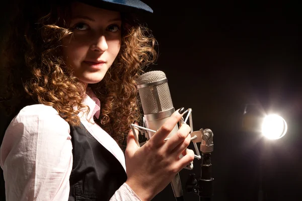 Belle chanteuse en chapeau avec microphone sur fond noir — Photo