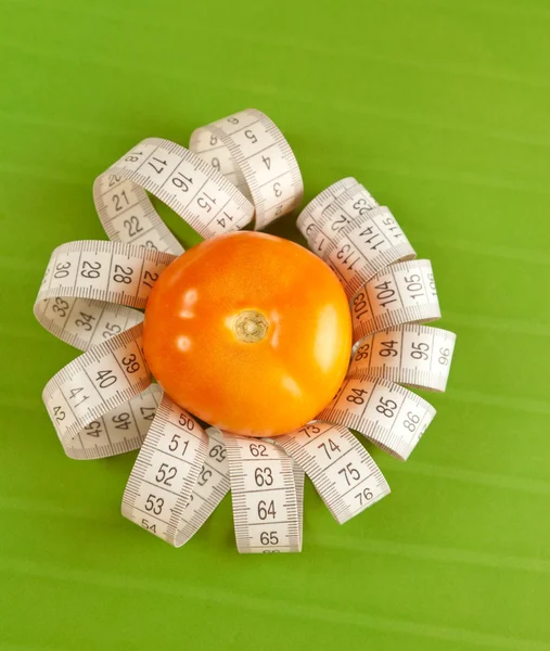 Picture of a tomato and tape measure on the green background — Stock Photo, Image