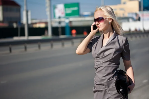 Woman in grey dress walking and calling by phone — Stock Photo, Image