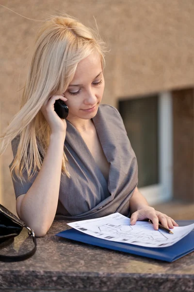 Mulher bonita sentado, ligando para o telefone e ler documentos — Fotografia de Stock