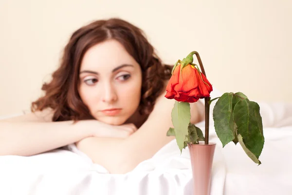 Nő az ágyban, látszó-on a rose (Rózsa összpontosítani) — Stock Fotó