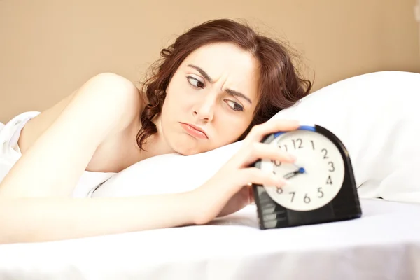 Woman lying a bed and holding an alarm (focus on woman) — Stock Photo, Image