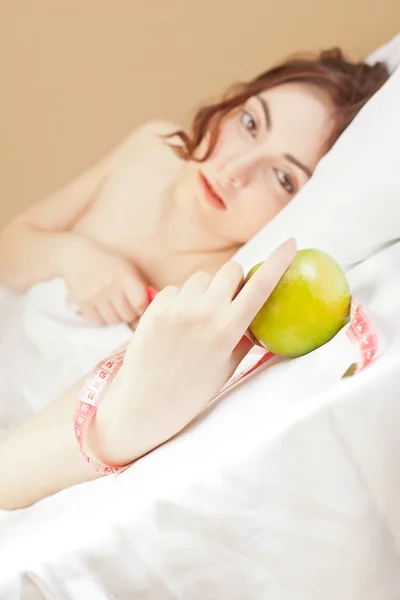 Piękna kobieta, leżąc w łóżku z zielonym jabłkiem — Zdjęcie stockowe