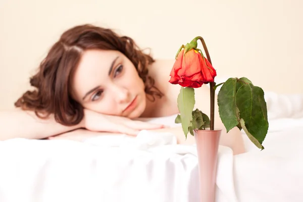 Жінка в ліжку дивиться на зів'ялу троянду (фокус на троянді ) — стокове фото