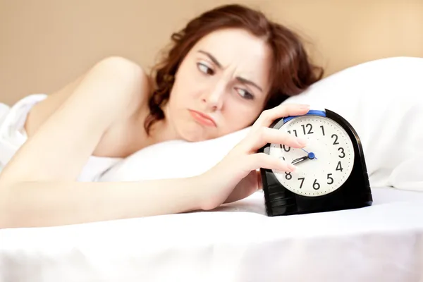 Kobieta, leżąc w łóżku i trzymając alarm (fokus na alarm) — Zdjęcie stockowe