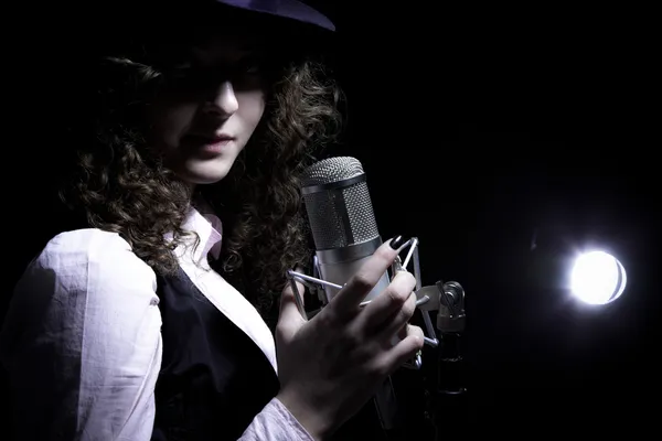 Bellissimo cantante in cappello con microfono sullo sfondo nero — Foto Stock