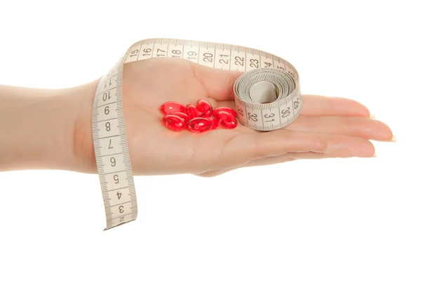 Женская рука с красными таблетками и рулеткой — стоковое фото