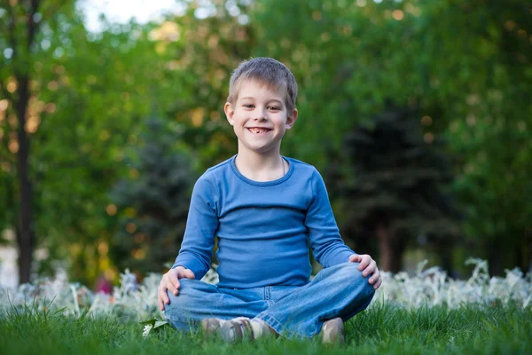 Boldog kisfiú ül a fűben — Stock Fotó