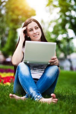dizüstü bilgisayar ile çim üzerinde oturan kız gülümseyerek